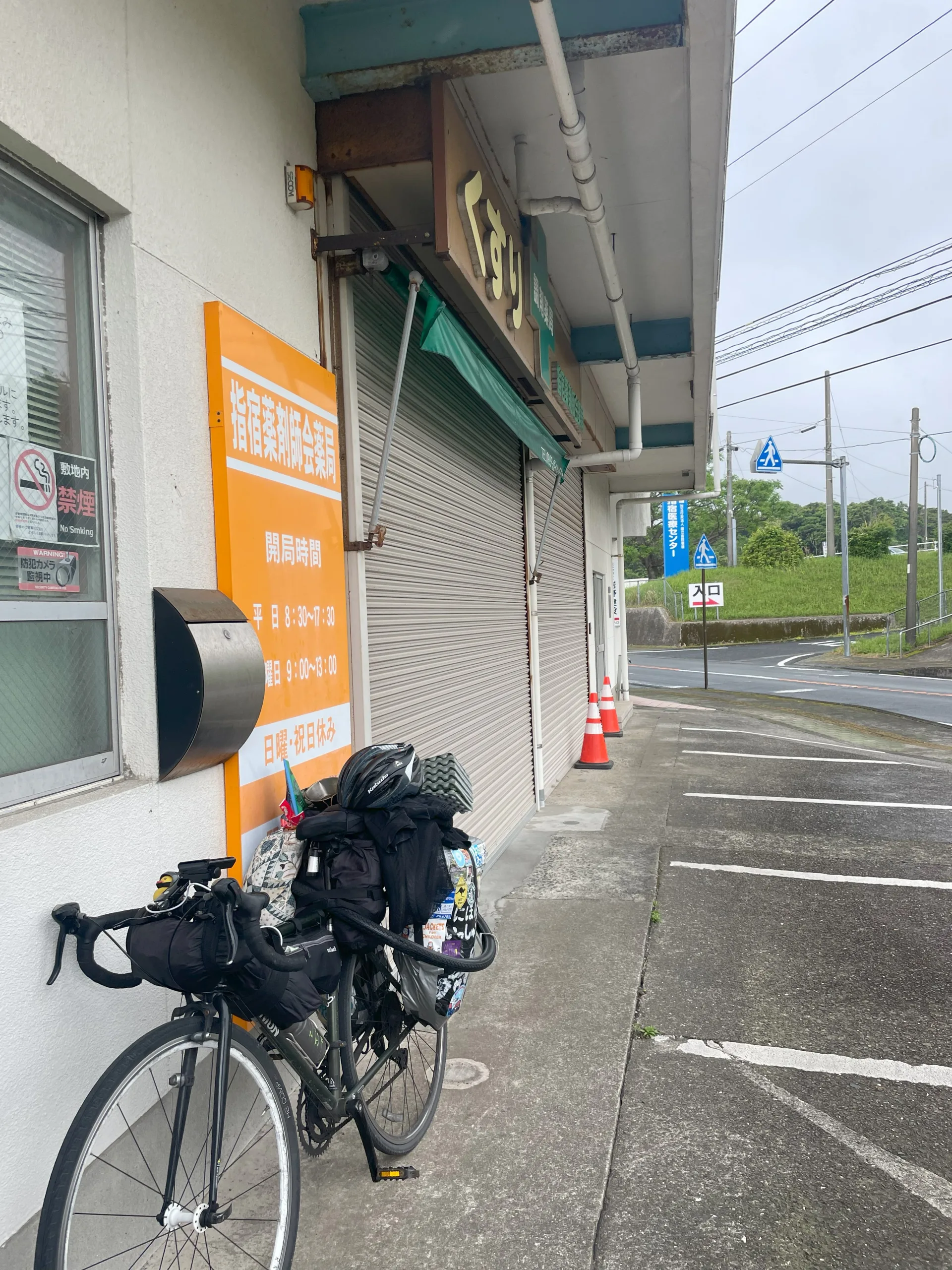 指宿市の薬局の屋根で雨宿りする自転車の旅人